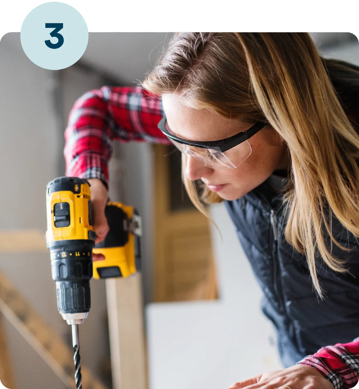 Woman using a drill with safety goggles to construct a Build&Bond DIY platform bed kit